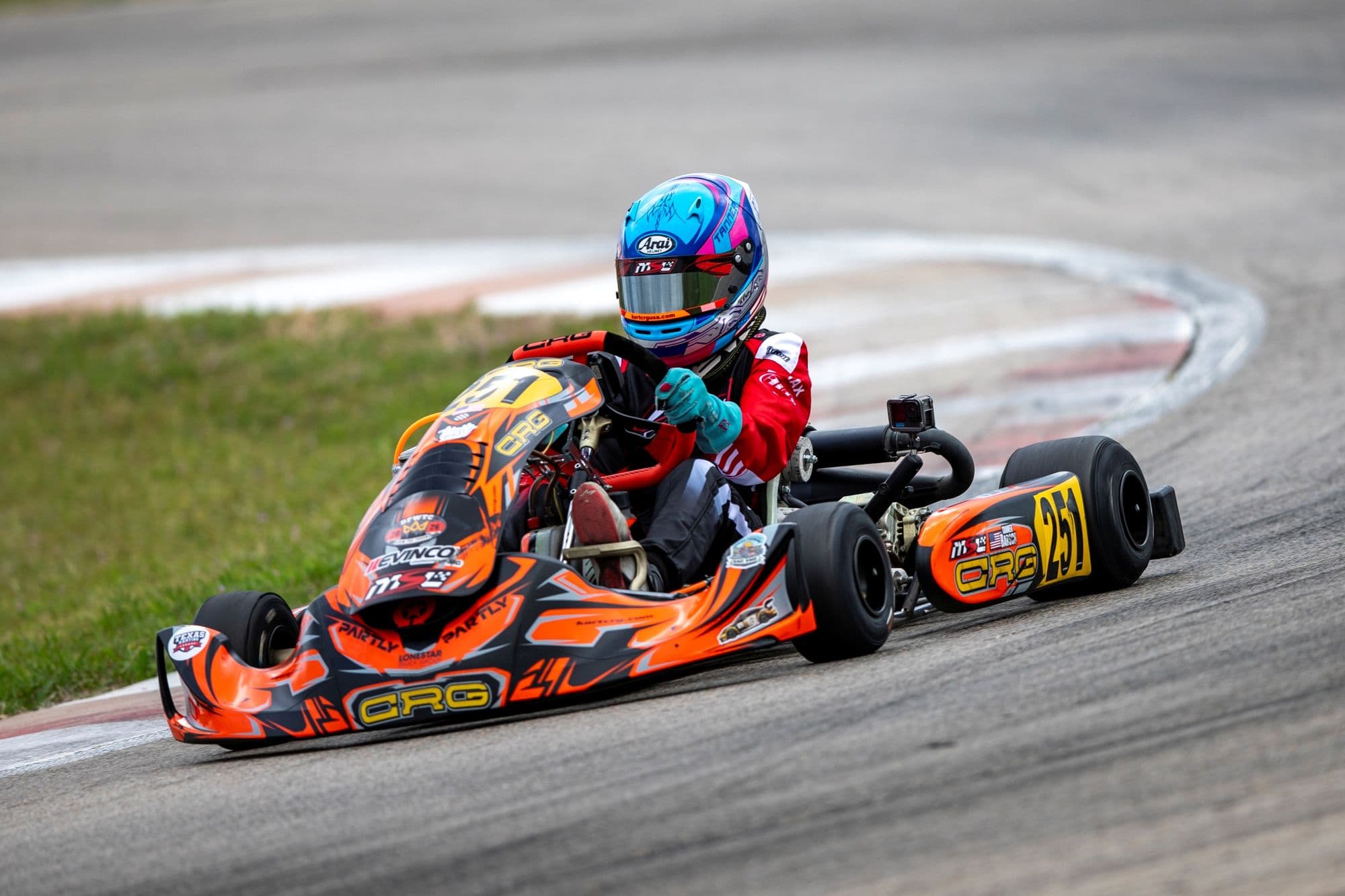 An orange kart with a blue helmet rides the curb mid-corner at KartMoto.