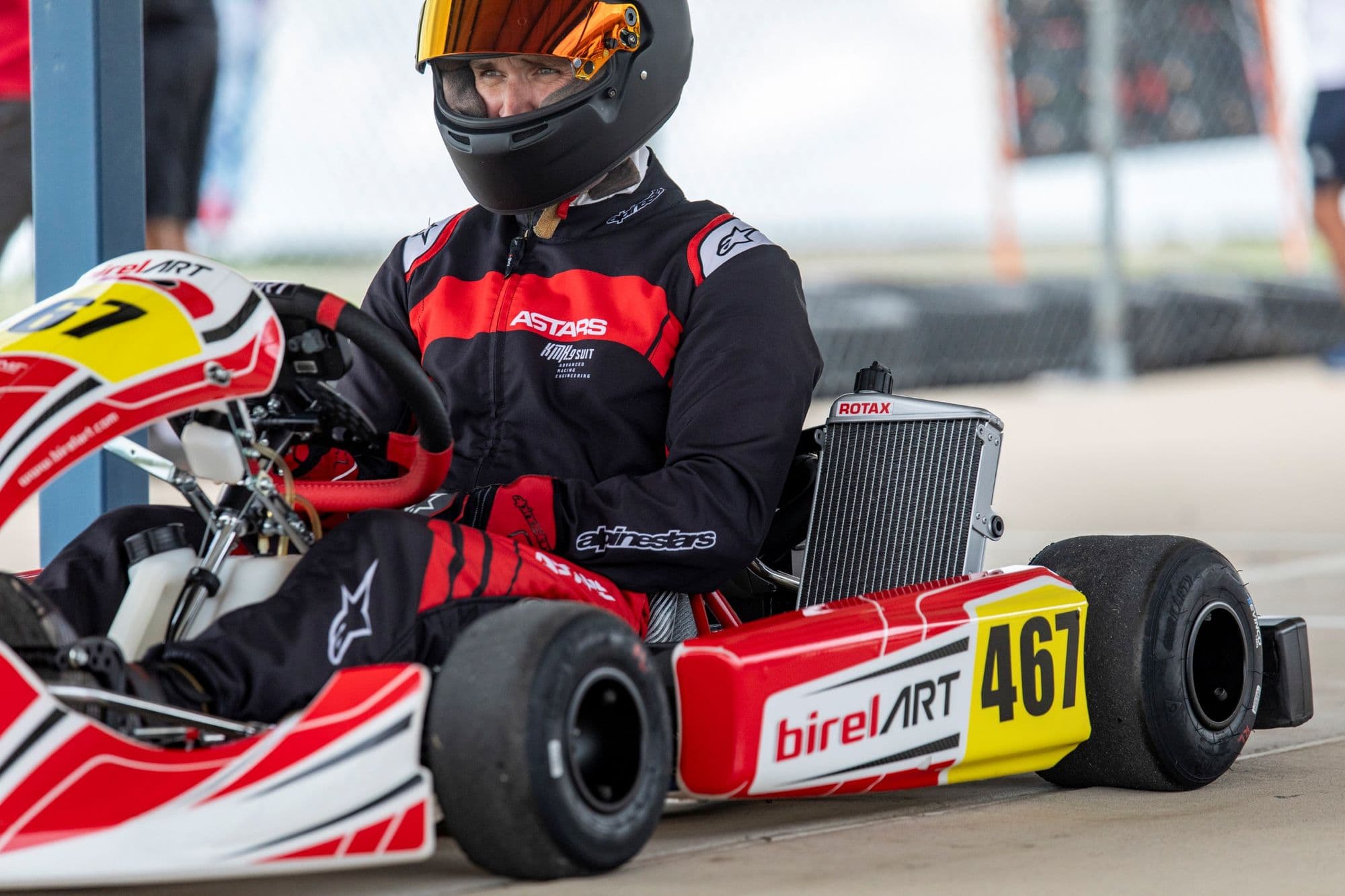 A driver in a red and black suit sits in a kart at KartMoto.