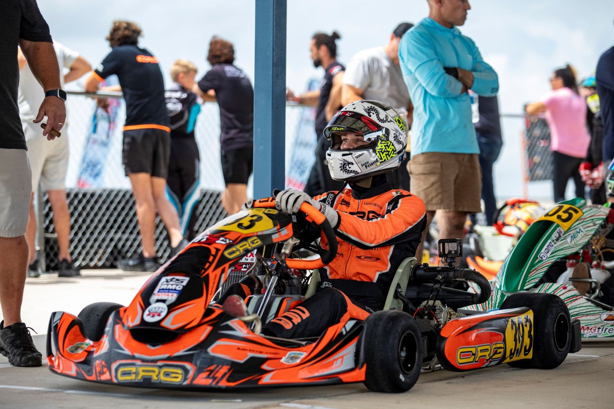 An orange kart in the pit lane at KartMoto with spectators behind the fence.