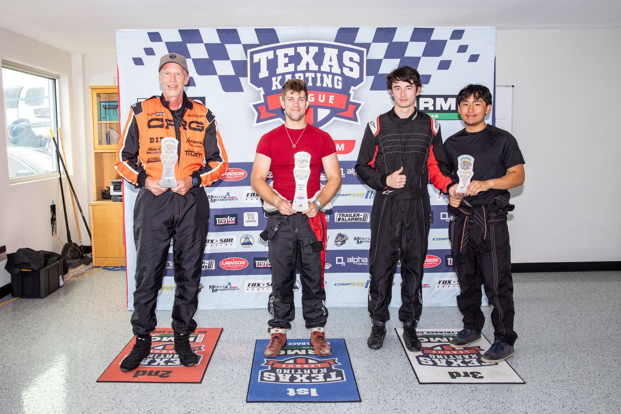 Four drivers hold trophies on the KartMoto podium.