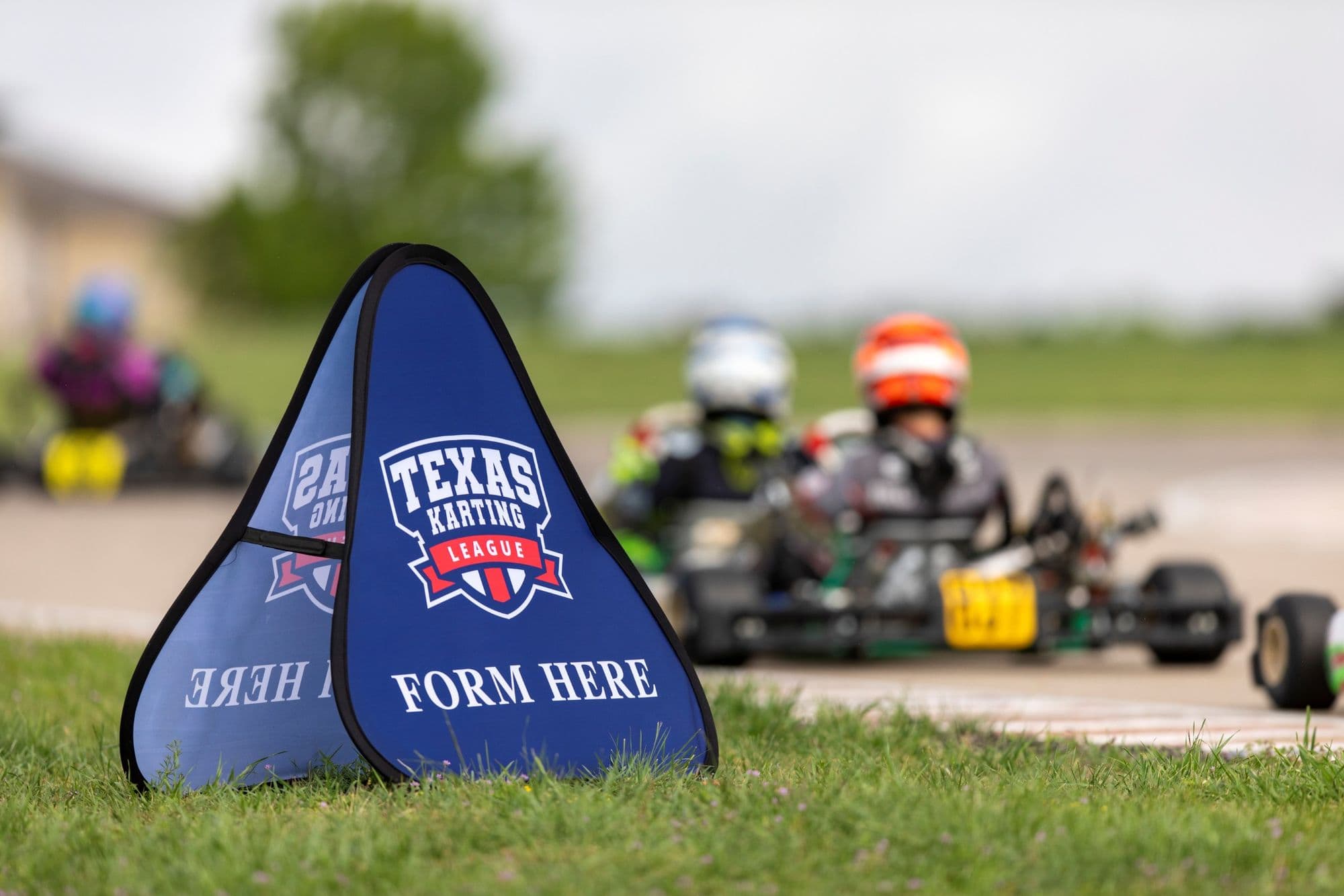 A Texas Karting League trackside sign with karts blurred behind it.