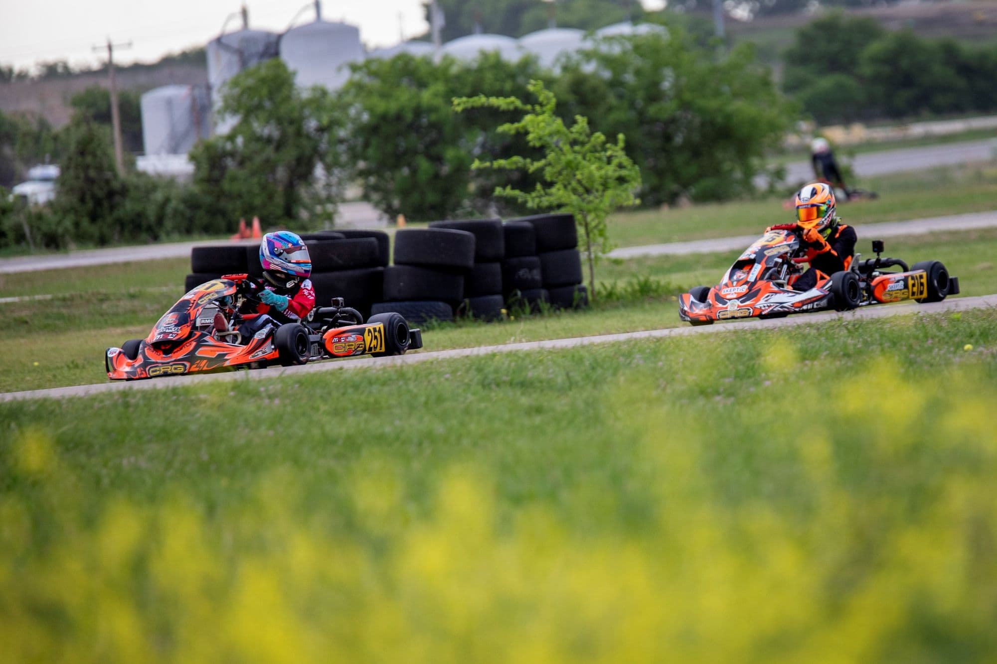 A pack of karts racing past yellow wildflowers at KartMoto.