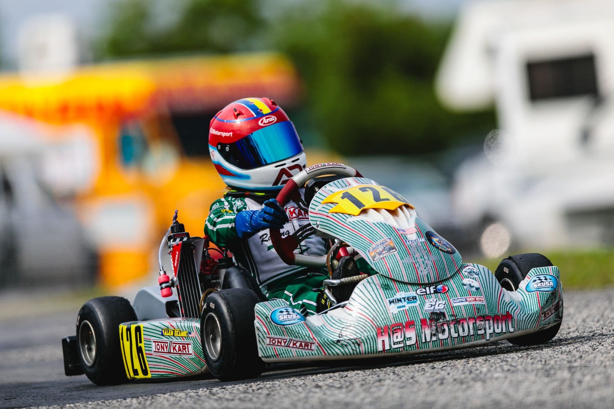 A teal kart comes head-on at GCKI Katy with a yellow bus in the background.
