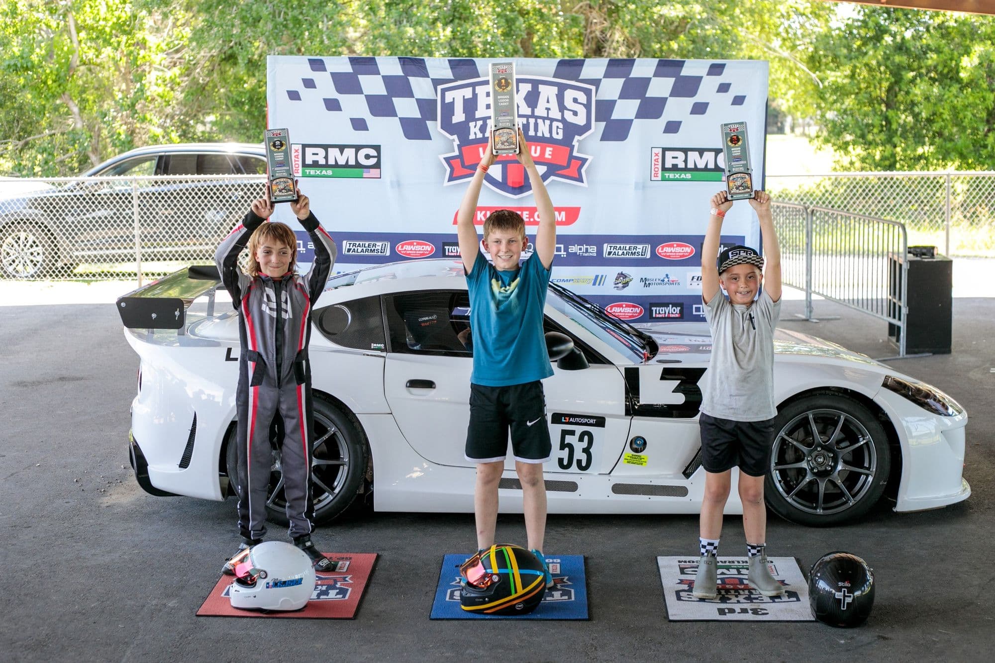 Three drivers with trophies on the GCKI Katy podium, in front of the TKL backdrop.