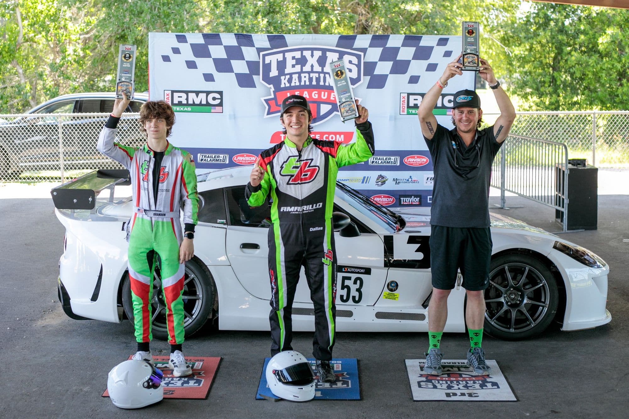 Three drivers in race suits celebrate with trophies at GCKI Katy.